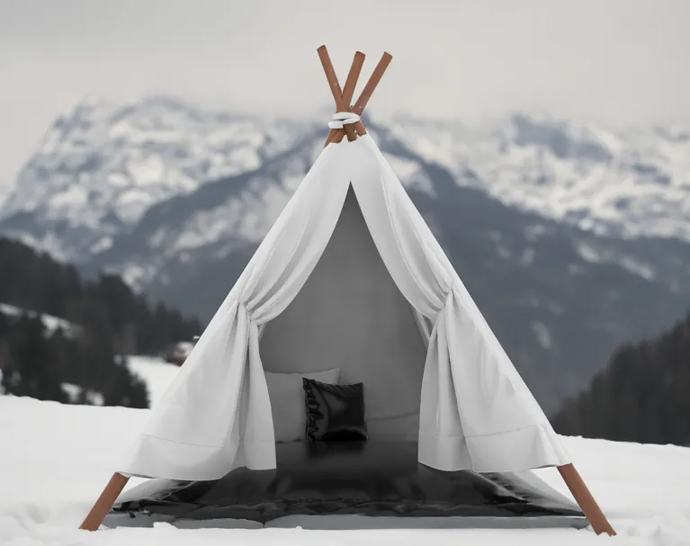 Weißes Tipi mit schwarzen Kissen vor verschneiten Berglandschaft