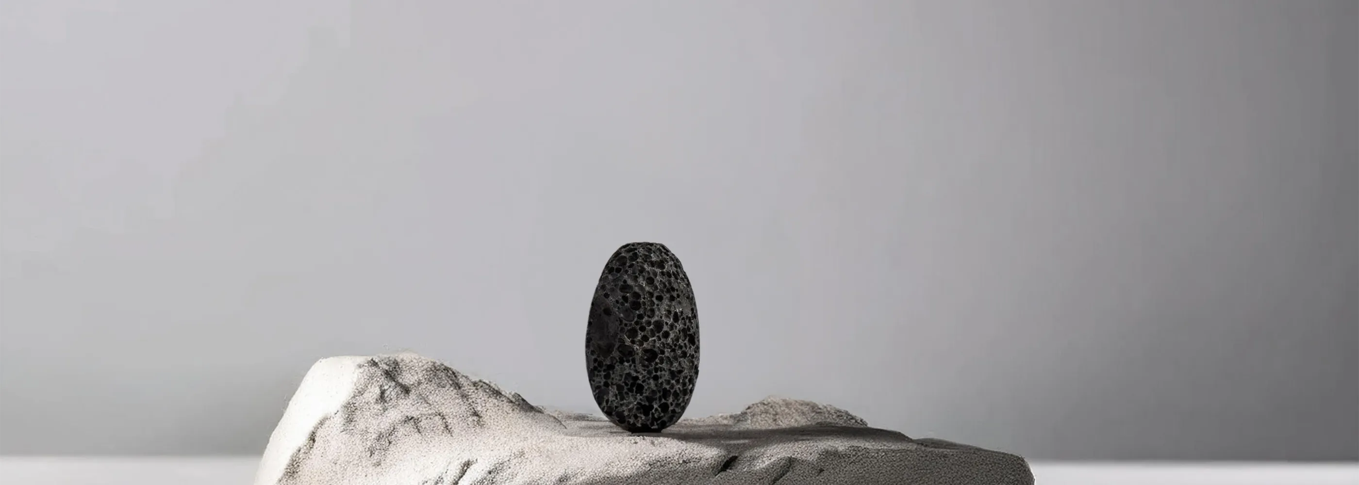 Schwarzer poröser Stein steht auf weißem Felsen in minimalistischer Umgebung