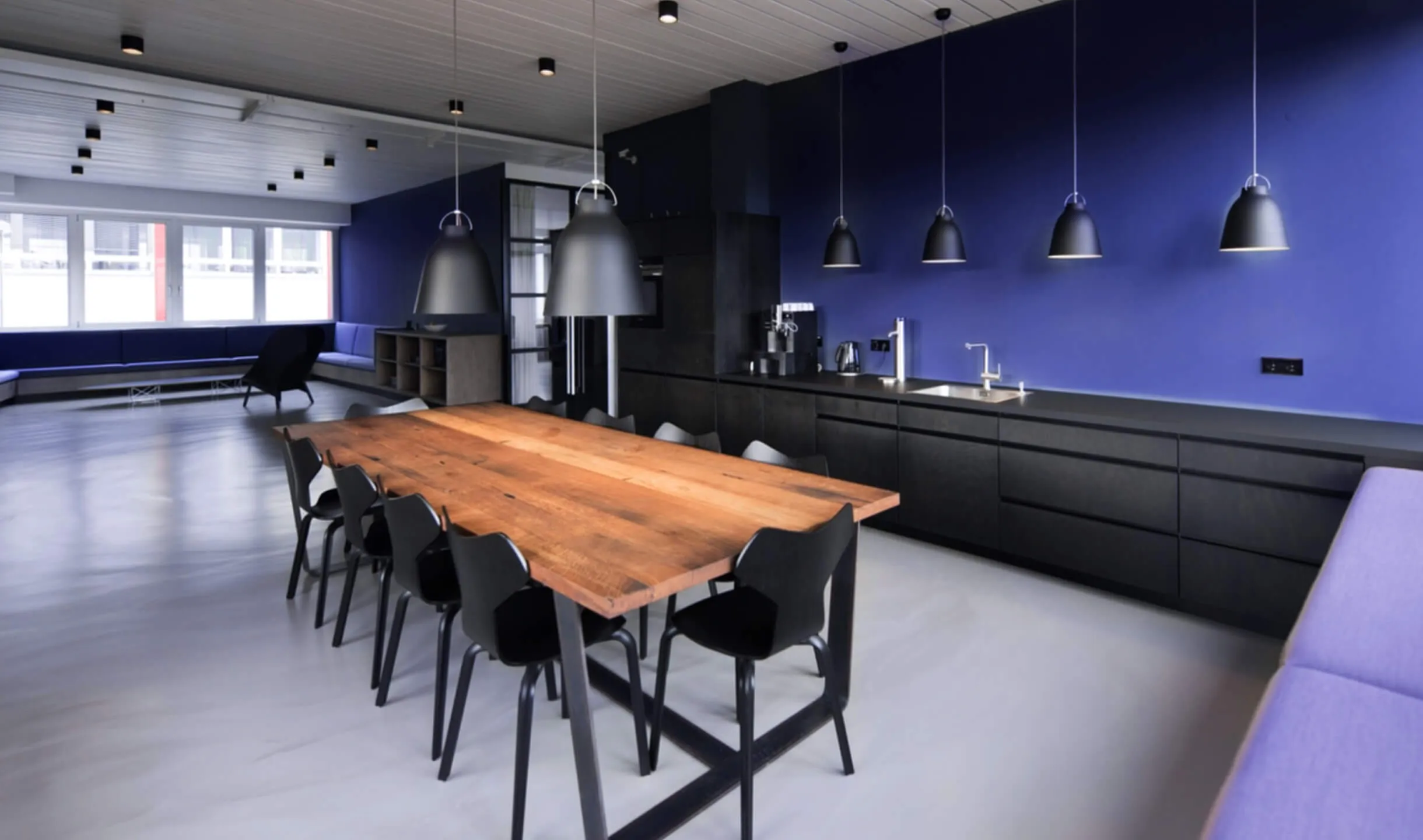 Moderne Küche mit blauer Wand, Holztisch und hängenden Designerlampen
